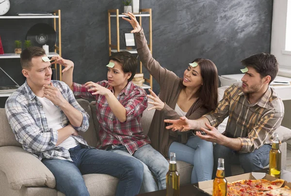 Compañía de jóvenes jugando con pegatinas en la frente . —  Fotos de Stock