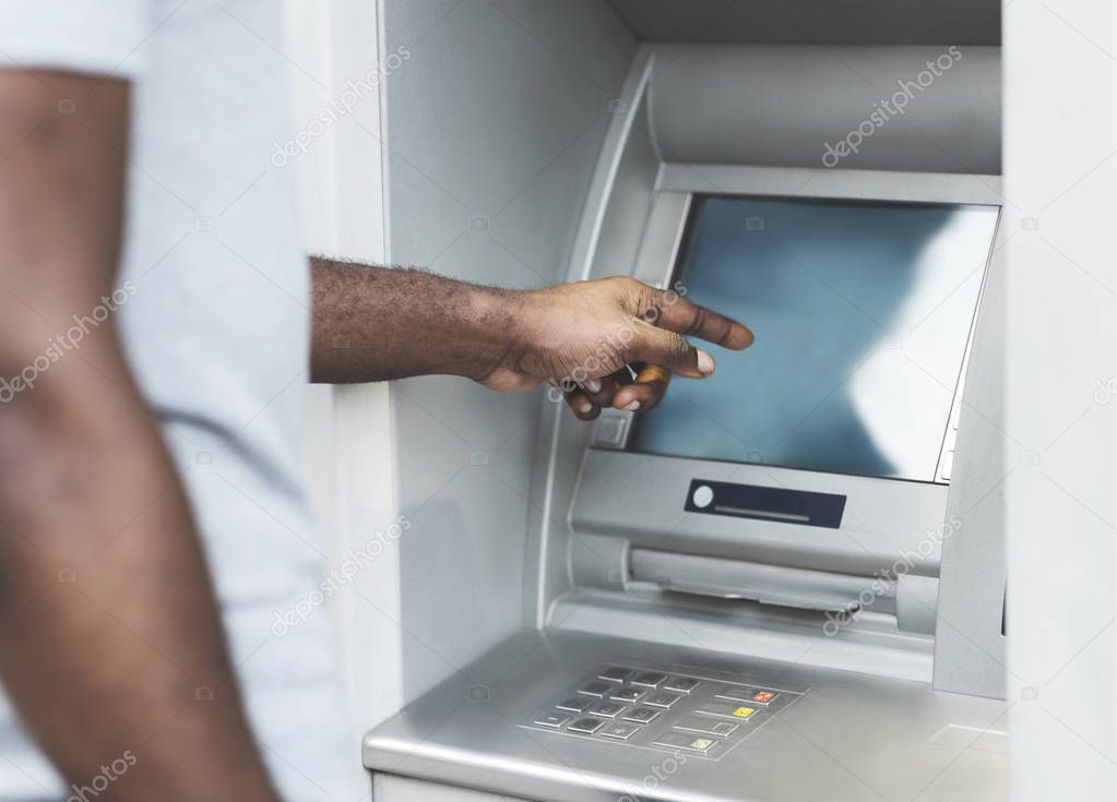 Unrecognizable African man using touch screen on ATM outdoor