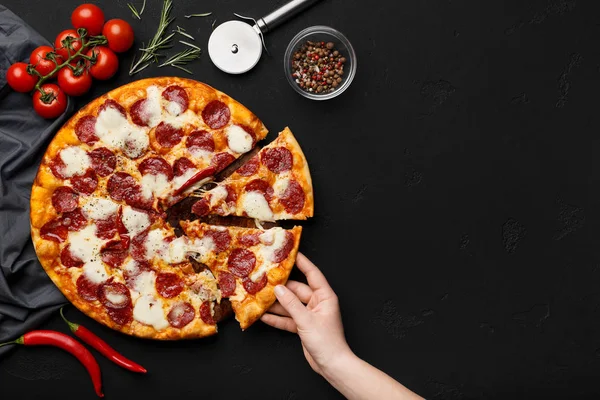 Donna che prende fetta di pizza al salame piccante sul tavolo nero — Foto Stock