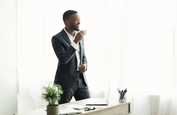 Hombre de negocios afroamericano guapo bebiendo café cerca de la ventana en la oficina — Foto de Stock