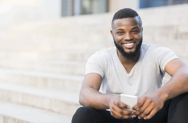 Glücklicher afrikanischer Kerl mit weißem breiten Lächeln, der draußen sitzt — Stockfoto