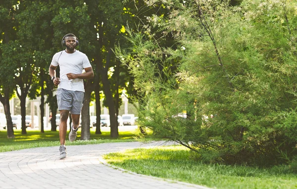 Sportlicher Afro-Typ mit Headset läuft im Park — Stockfoto