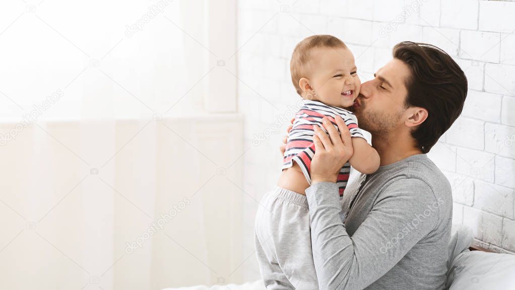 Young man kissing his adorable baby son, enjoying babysitting