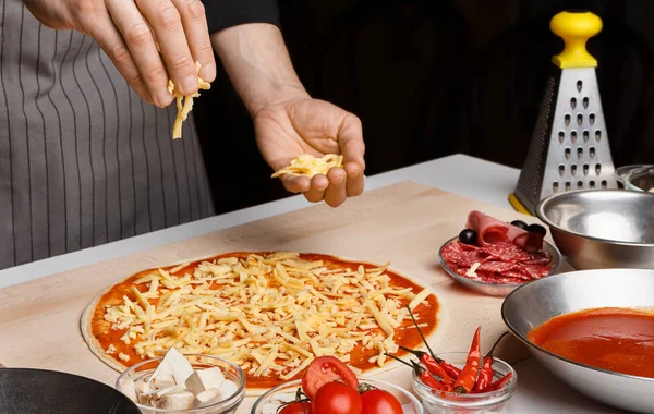 Chef preparing pizza, adding cheese to pizza base — Stock Photo, Image