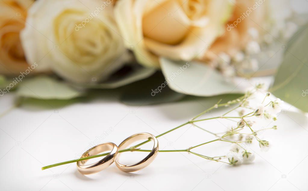 Pair of wedding gold rings with dry flowers and roses on white