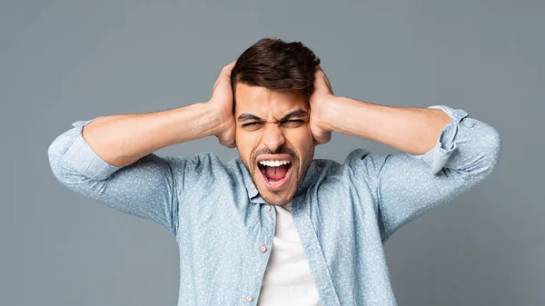 Emotionaler hispanischer Mann, der vor grauem Hintergrund schreit und seine Ohren verdeckt — Stockfoto