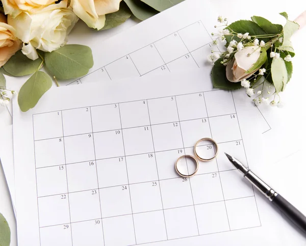 Planowanie daty ślubu w kalendarzu ze złotymi pierścieniami i róż — Zdjęcie stockowe