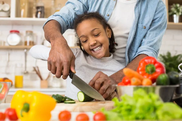 Küçük afro kız babasının yardımıyla salatalık kesiyor — Stok fotoğraf