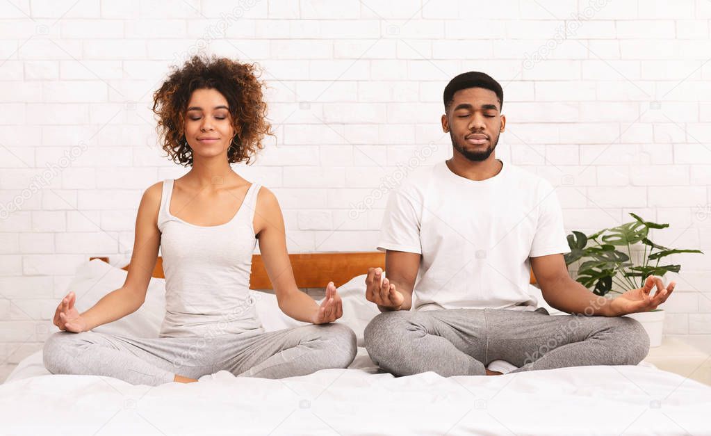 Young black family meditating in bed together