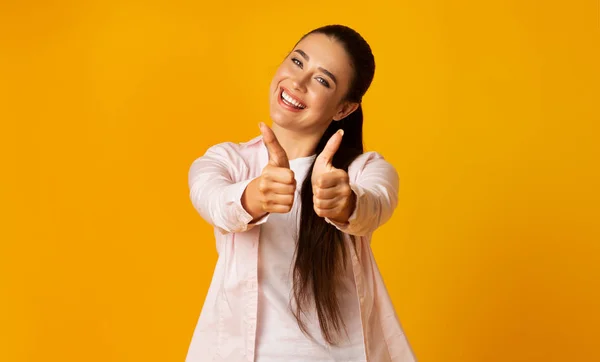 Emocionado morena chica gestos pulgar hacia arriba sobre amarillo fondo —  Fotos de Stock