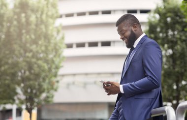 Çekici işadamı cep telefonu yla mesajlaşma, modern ofis binası yakınında duran