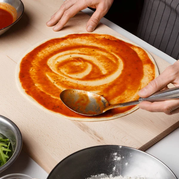 Man adding tomato sauce on pizza base, closeup — Stock Photo, Image