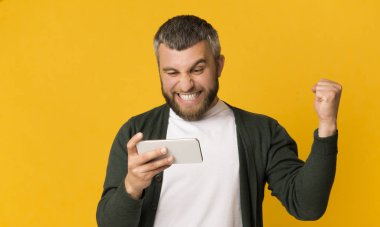 Heyecanlı sakallı adam akıllı telefon tutan ve yumruk sıkma