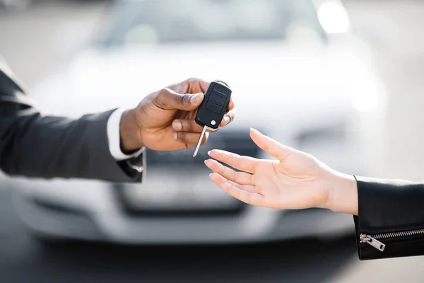 Car salesman handing over keys for new car to young woman