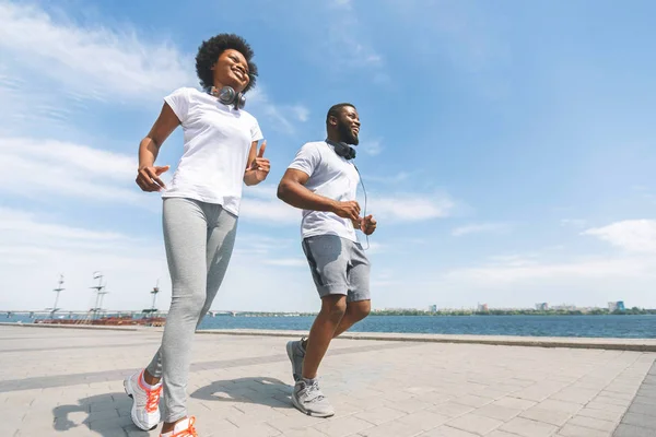 Alegre afro pareja corriendo a lo largo de río ribera en ciudad, bajo ángulo disparo —  Fotos de Stock