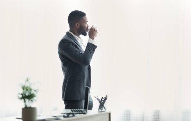 Yakışıklı Afro-Amerikan işadamı ofiste pencere yakınında kahve içme