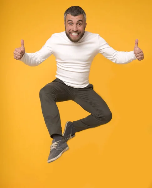 Радостный кавказский мужчина, прыгающий в воздух с большими пальцами вверх — стоковое фото