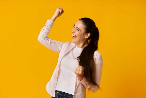 Jolie brune fille secouant les poings célébrant le succès sur fond jaune — Photo