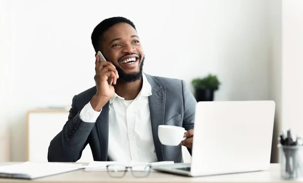 Homem de negócios preto falando no telefone celular e trabalhando no laptop — Fotografia de Stock