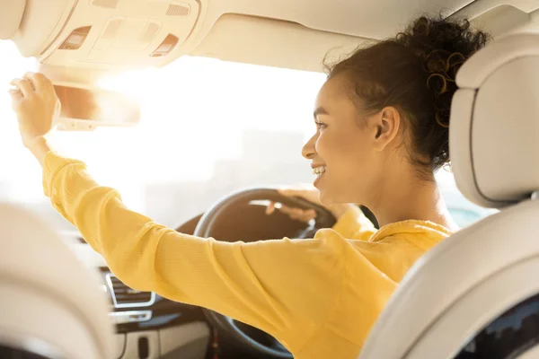 Счастливая девушка трогает зеркало заднего вида, вождение автомобиля — стоковое фото