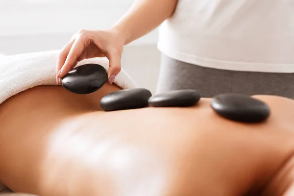 Massagista fazendo pedras quentes massagem para cliente feminino — Fotografia de Stock