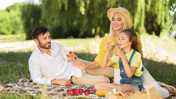 Девочка пускает пузыри наслаждаясь днем с родителями в парке — стоковое фото