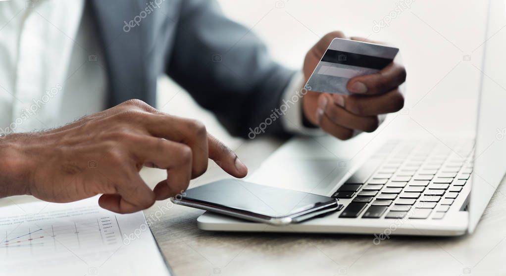 African businessman booking tickets online using smartphone, holding credit card.