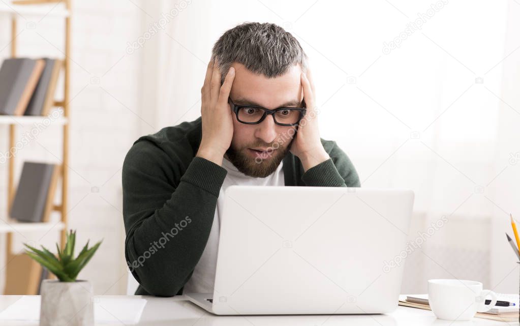 Shocked caucasian man is sitting in front of laptop
