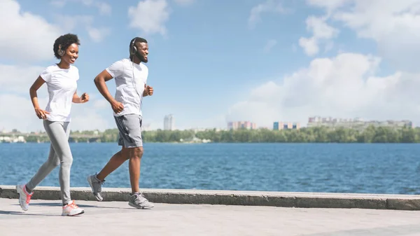 Glad afrikansk amerikansk par jogging längs floden Embankment i staden — Stockfoto