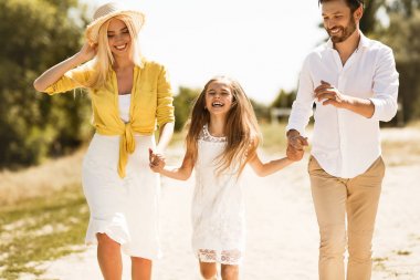 Mutlu ebeveynler kızıyla yürürken, el ele tutuşarak