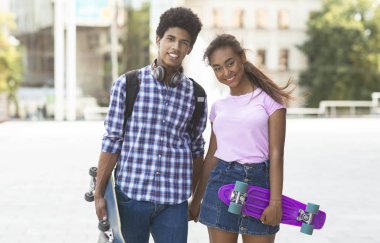 Modern kaykaylar el ele tutuşan, kameraya poz gülümseyen gençler