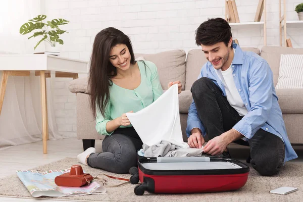 Jeune couple emballant des vêtements dans une valise à la maison — Photo