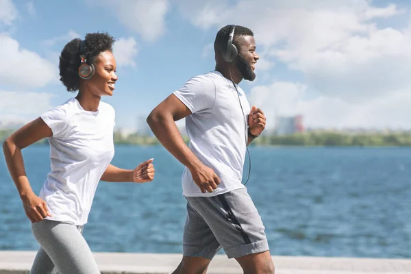 Positivo afro coppia jogging lungo fiume embbankment in città — Foto Stock