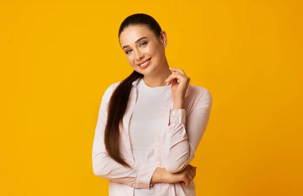 Atractiva mujer joven sonriendo mirando a la cámara en el fondo amarillo —  Fotos de Stock