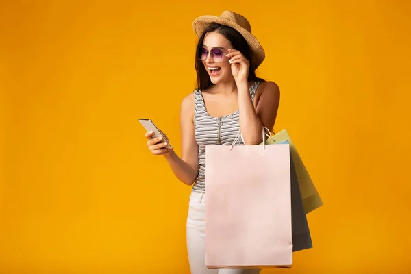 Sarı Arka Planda Renkli Alışveriş Çantaları Tutan Cep Telefonu Kullanan Kız — Stok fotoğraf