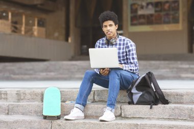 Yakışıklı siyah genç dizüstü bilgisayar ile merdivenlerde oturan
