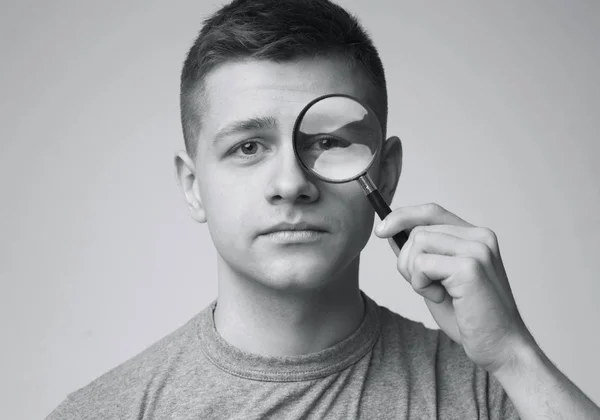 Porträt eines jungen Mannes, der durch ein Vergrößerungsglas schaut — Stockfoto