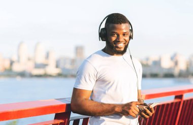 Siyah gülümseyen koşucu eğitim için hazırlanıyor, cep telefonu tutarak