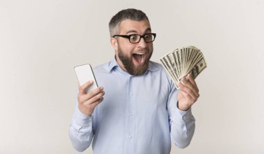 Excited man holding smartphone and looking at bunch of money clipart
