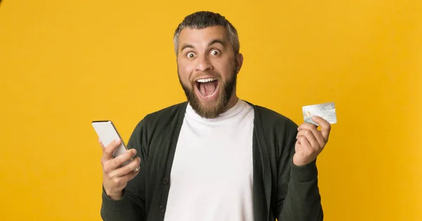 Homem emocional segurando cartão de crédito e smartphone — Fotografia de Stock