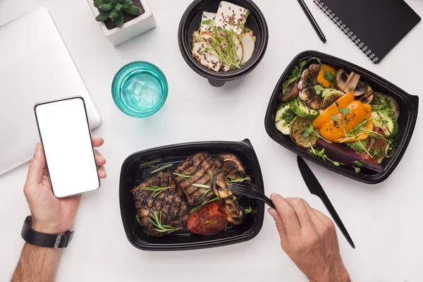 Man eating healthy food in to go boxes and holding cellphone