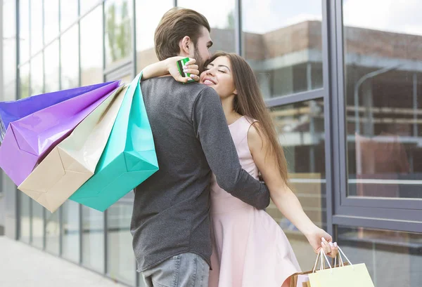 Young caucasian shoppers hugging with shopping bags and credit card — Stock Photo, Image