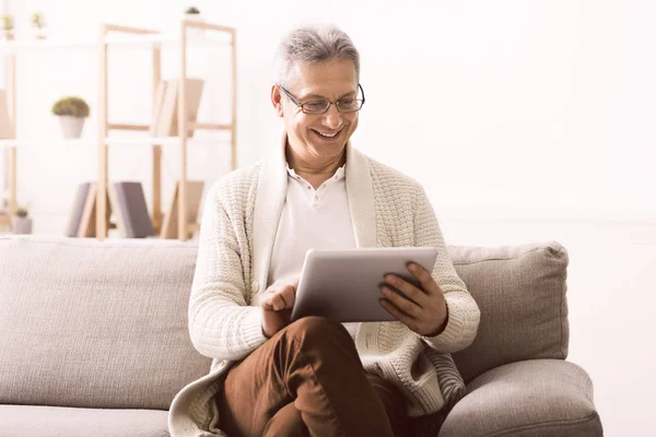 Senior férfi néz fénykép-ra tabletta otthon — Stock Fotó
