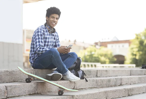 Adolescente alegre usando smartphone sentado em escadas contra a paisagem urbana — Fotografia de Stock