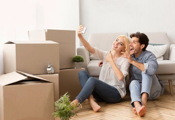 Casal feliz fazendo selfie entre caixas móveis no novo apartamento — Fotografia de Stock