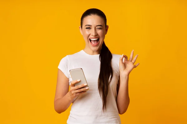 Gorgeous Woman Gesturing OK And Holding Cellphone On Yellow Background — Stock Photo, Image