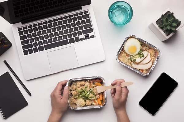 Woman eating healthy food in foil boxes in office with laptop — Stock Photo, Image