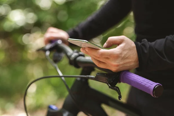 Przycięte imafe rowerzysty trzyma rower i za pomocą smartfona — Zdjęcie stockowe