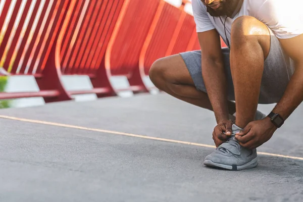 Afrikanischer Jogger überprüft seine Schnürsenkel auf Brücke — Stockfoto