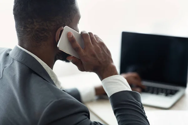 Homme d'affaires noir parlant sur un téléphone mobile et travaillant sur un ordinateur portable au bureau — Photo
